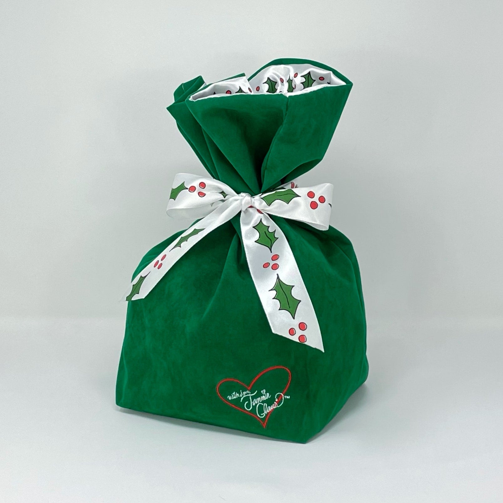 Jammie Claus Signature Bag that is green with a white bow that has holly printed on it and the bag as the Jammie Claus heart logo